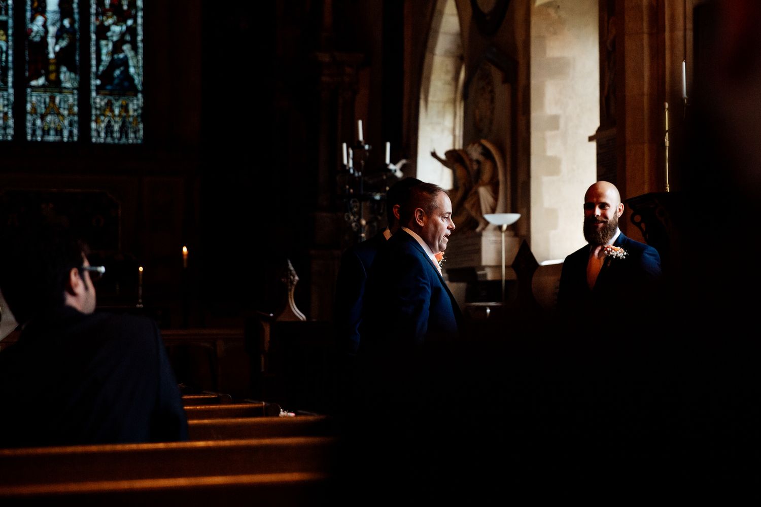 Wedding ceremony attendees gather in a dimly lit church interior with ornate architectural details.