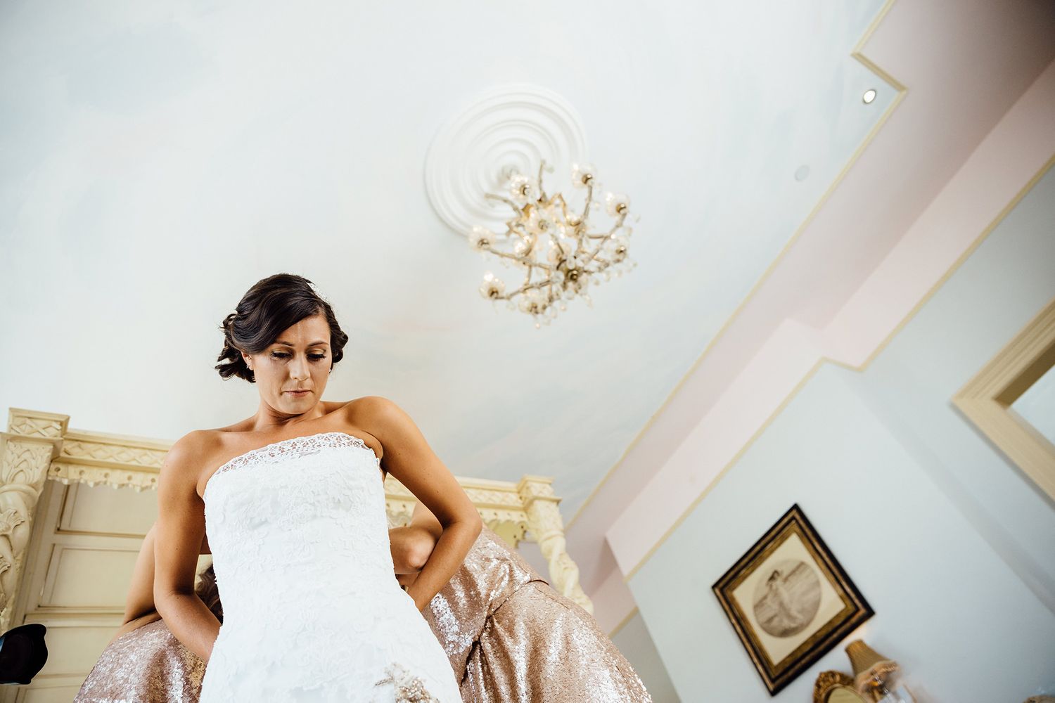 Elegant chandelier hangs from white ceiling during wedding preparations.