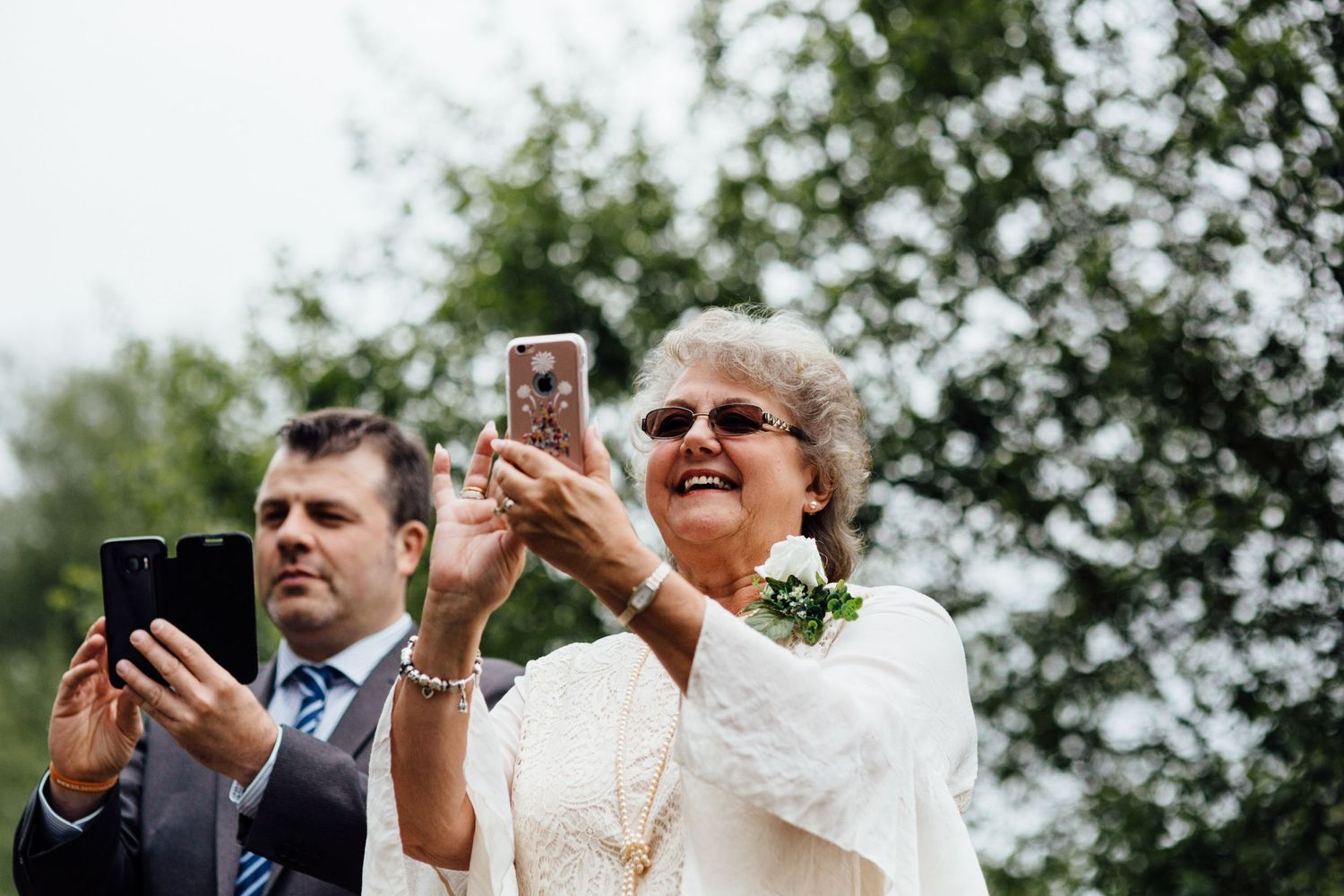 Wedding party members take photos with smartphones outdoors.
