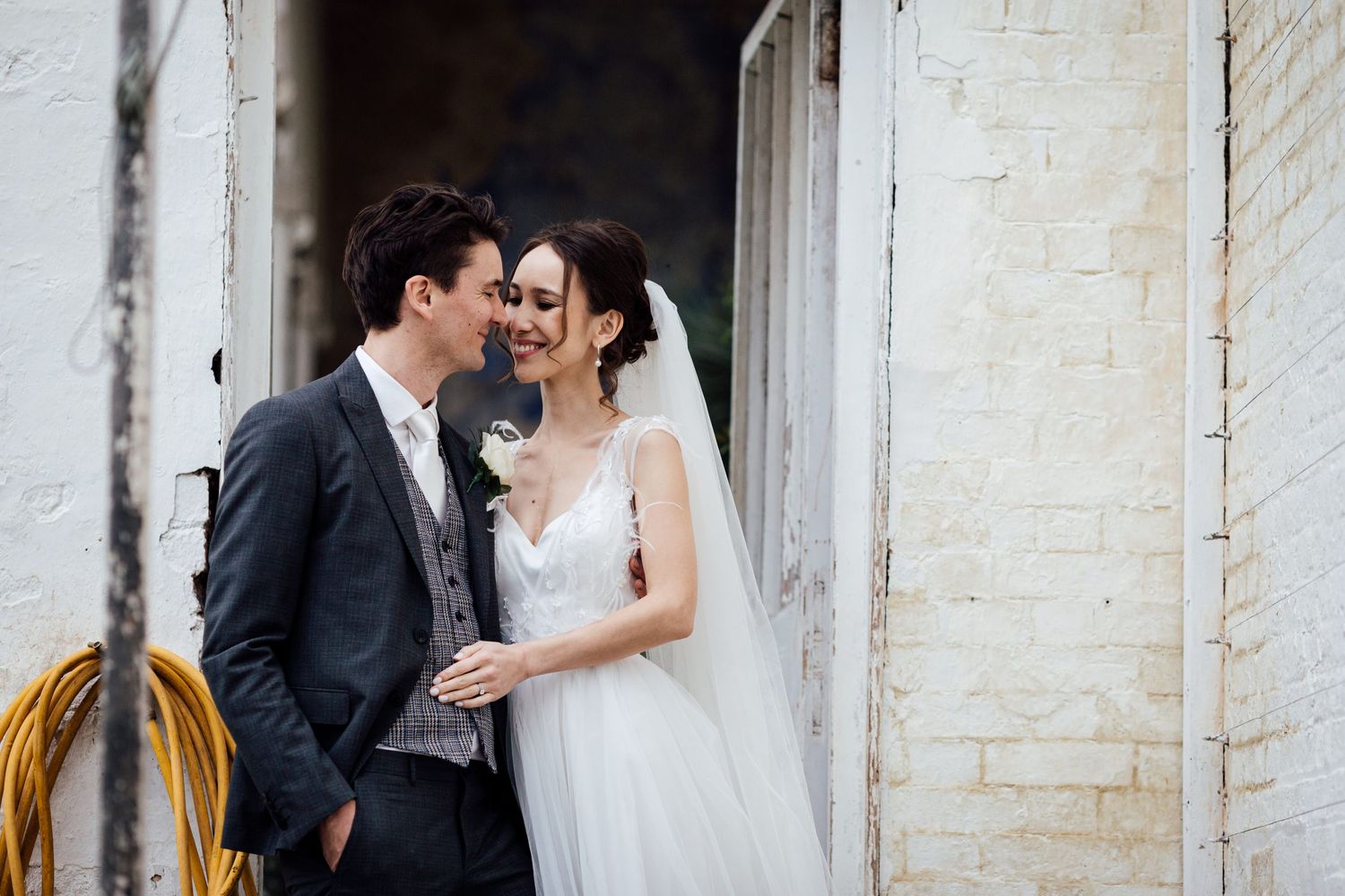Romantic wedding portrait against white brick wall backdrop.