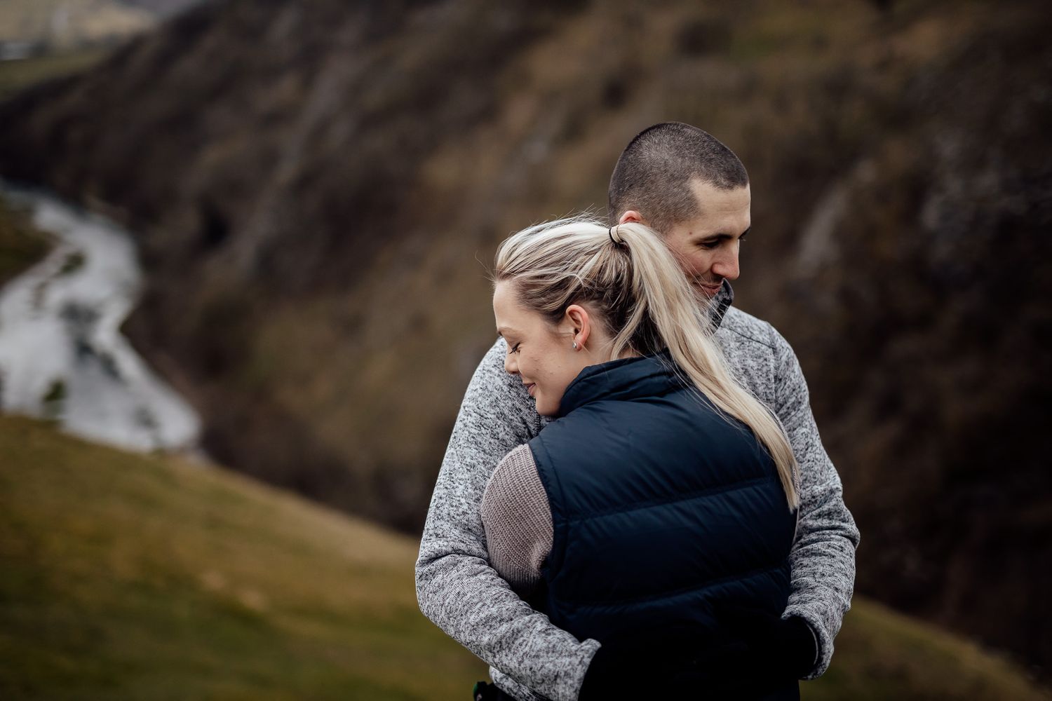 A couple embraces intimately against a rugged mountain backdrop during their engagement session.
