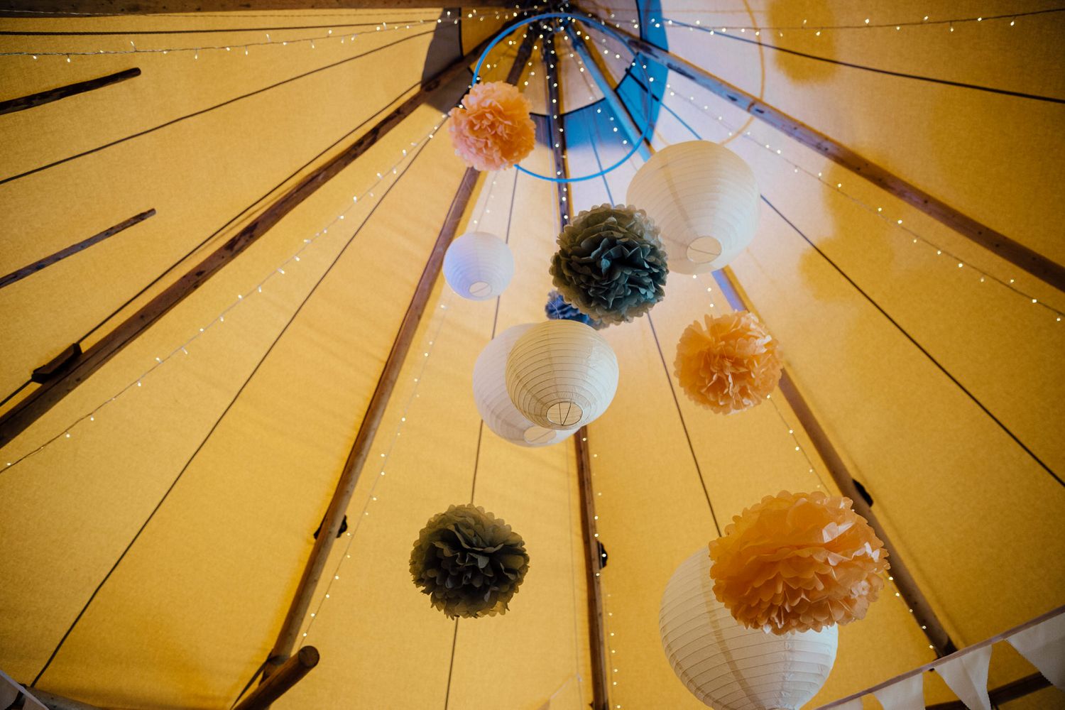 Decorative paper pom poms hang from wooden beams in a rustic wedding venue.