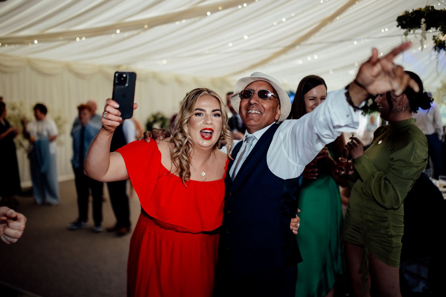 Wedding reception tent with guests dancing and celebrating under string lights.