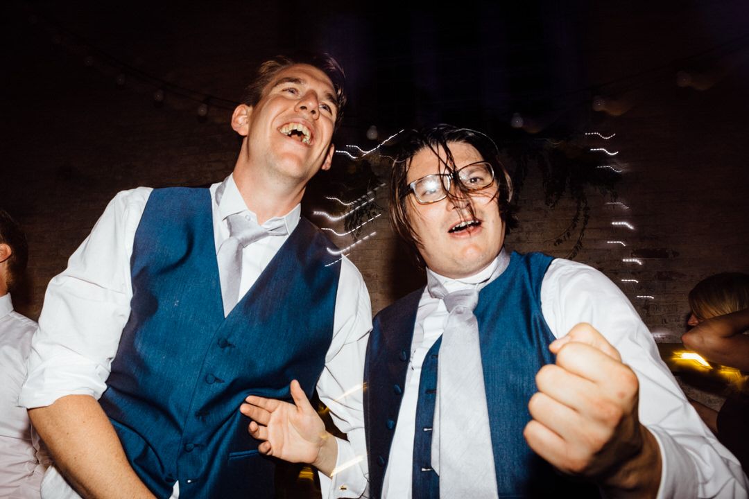 Two wedding guests in blue vests dancing enthusiastically at reception.