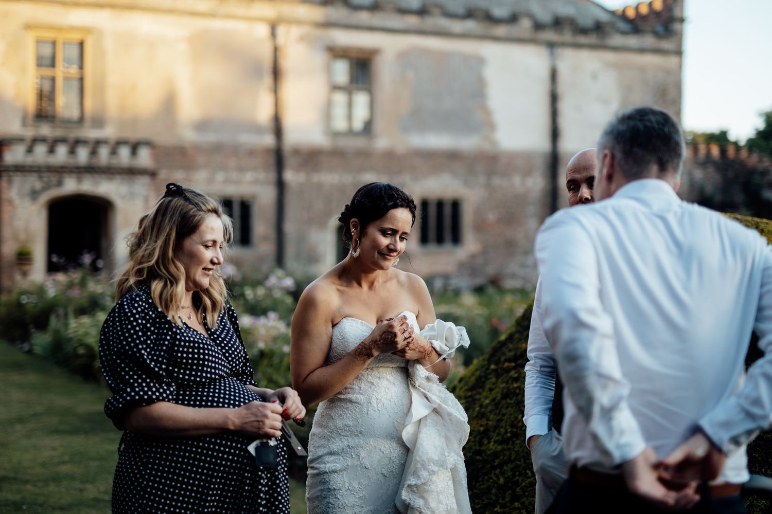 Wedding guests gathered on a lawn outside a historic stone building at sunset.