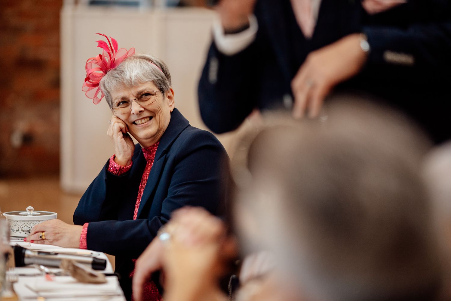 A wedding guest wearing a bright red fascinator smiles during the reception.