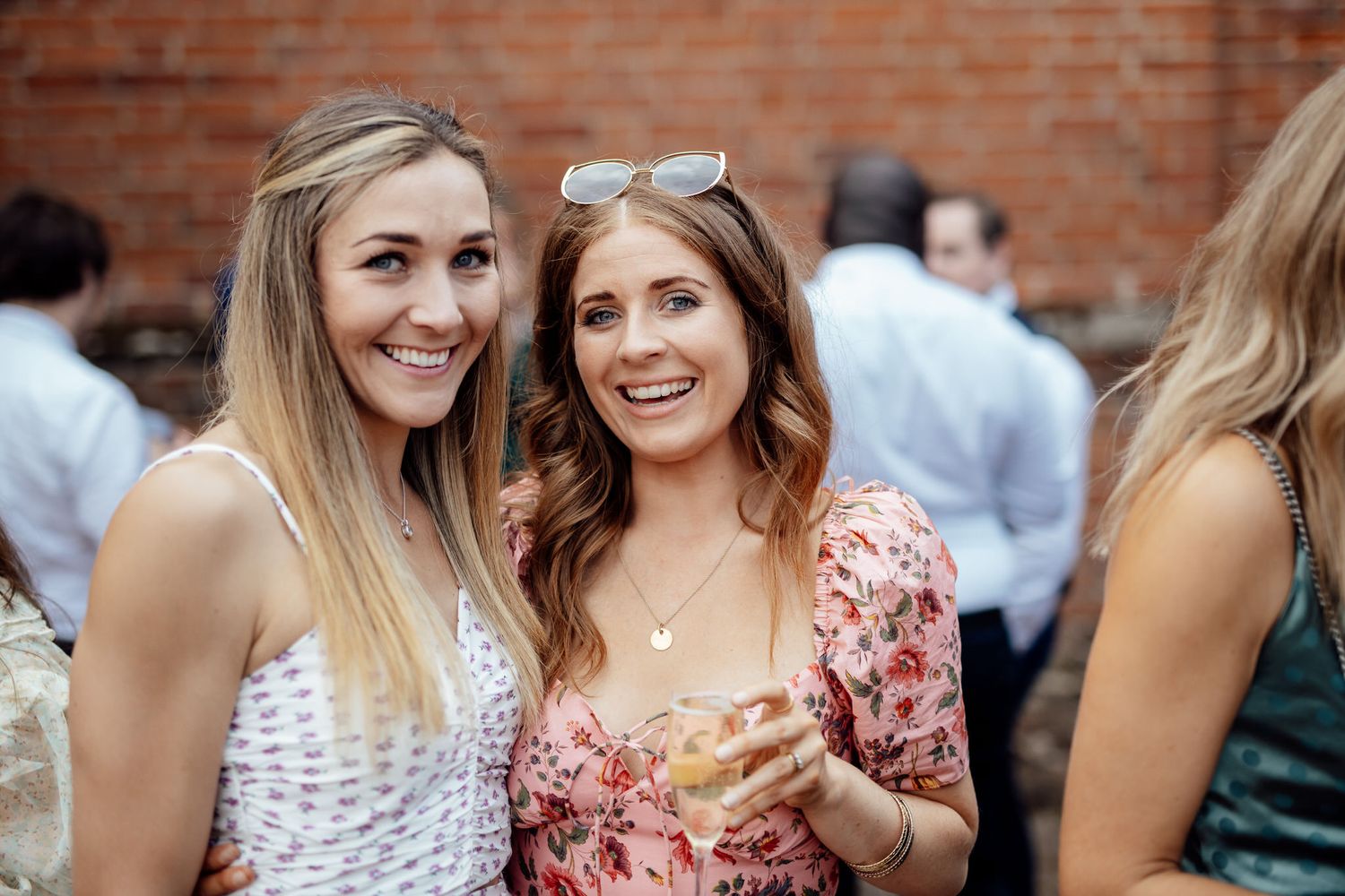Wedding guests enjoying refreshments at an outdoor reception with brick wall backdrop.