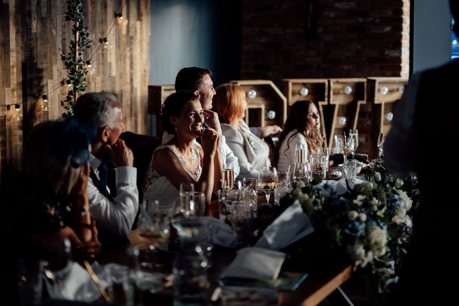 Dark and moody indoor reception scene with tables set for a wedding celebration.