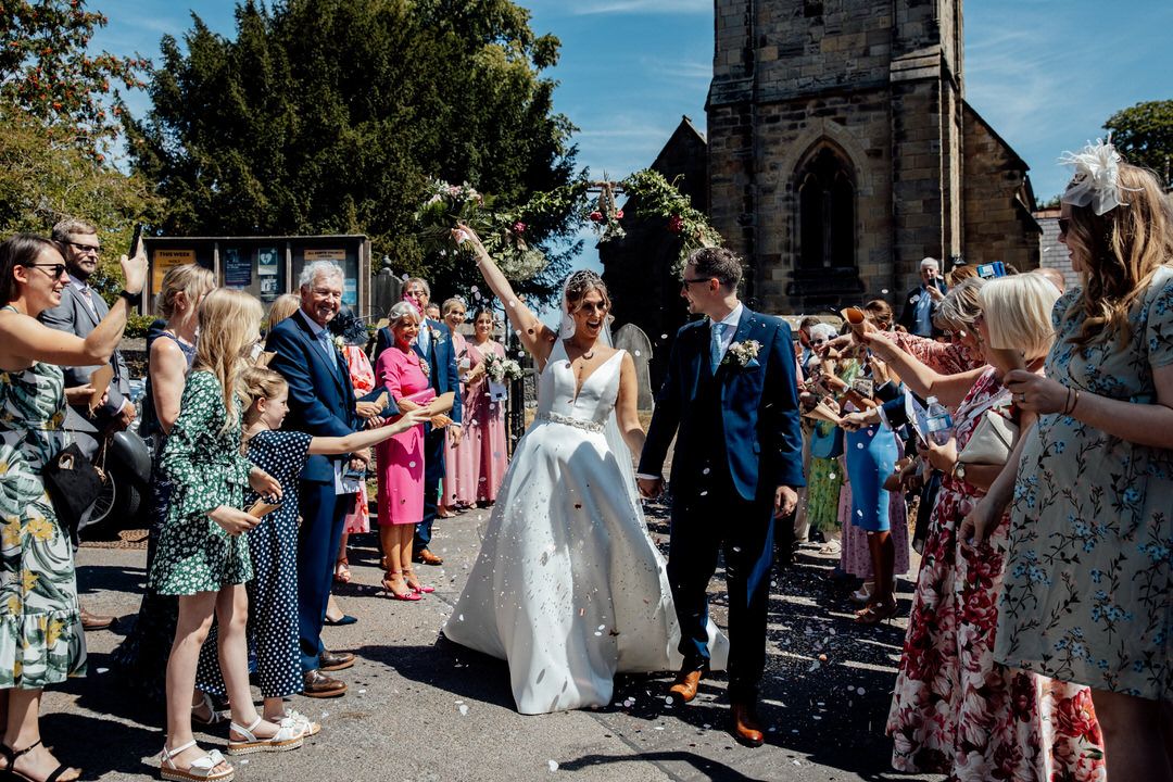 Panoramic view of wedding guests lining up outside a church for the confetti throw.
