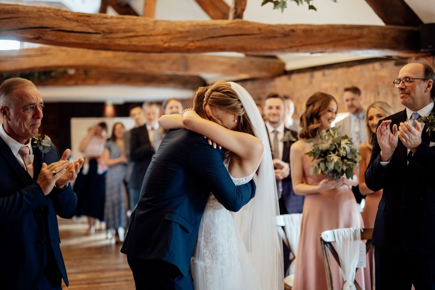 Wedding guests celebrate during a joyful reception in a rustic wooden beam venue.