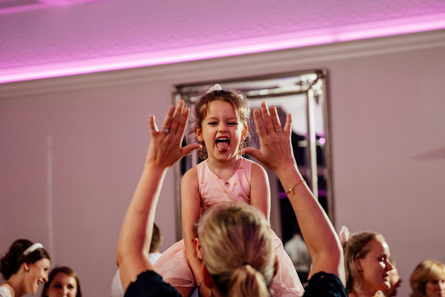 Celebration crowd with raised hands dancing under pink and purple mood lighting.