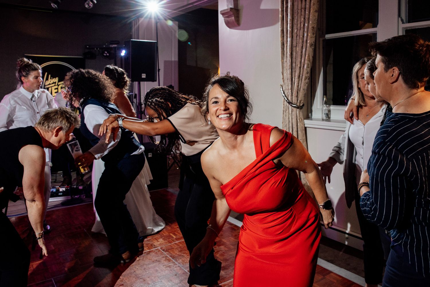 Wedding reception dance party with guests celebrating under pink and purple lighting.
