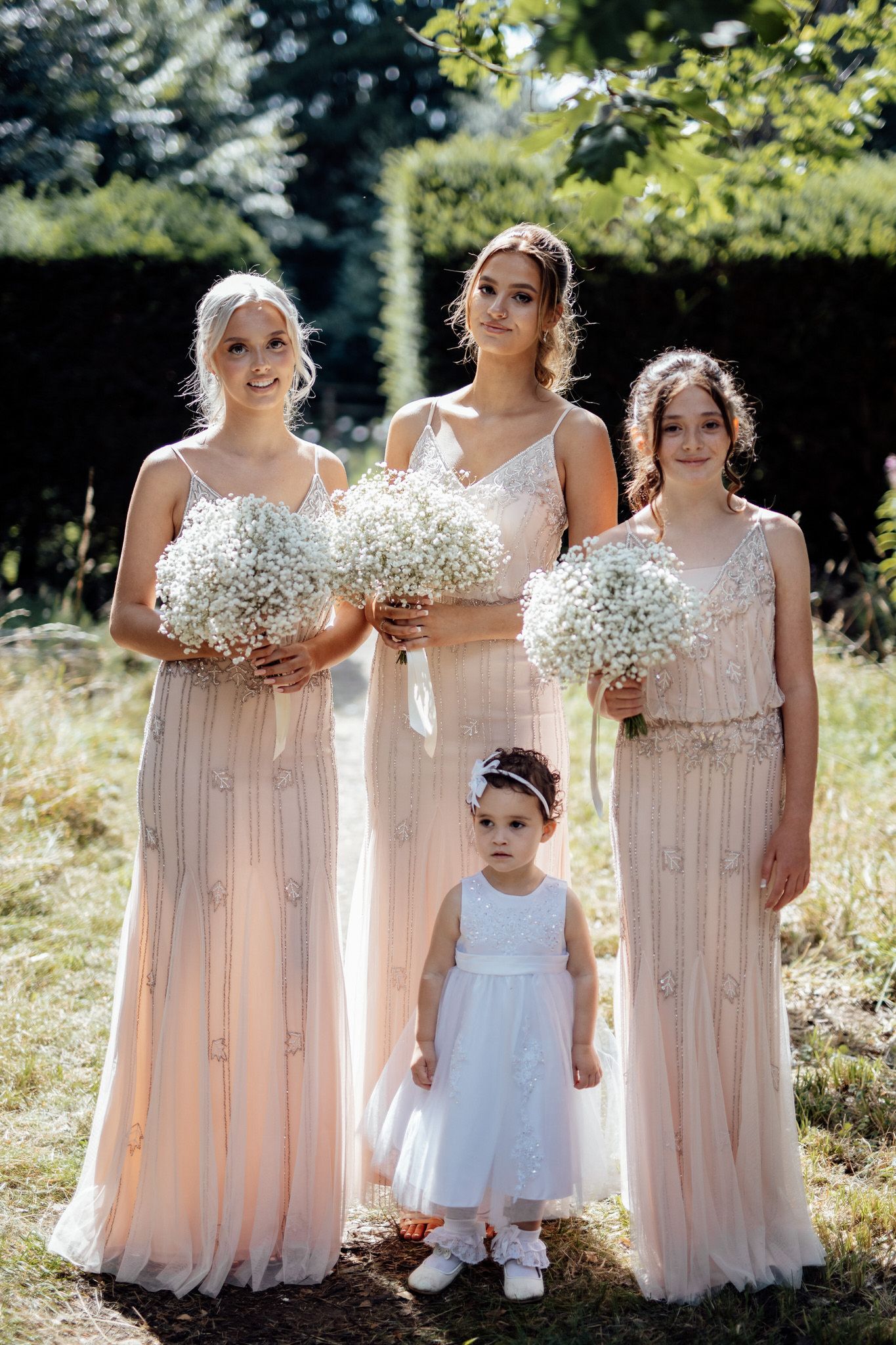 Bridesmaids in blush pink dresses holding baby's breath bouquets pose together outdoors.