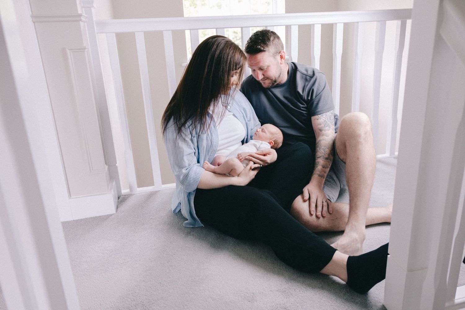 Parents sitting on floor of nursery admiring their newborn baby wrapped in white blanket.