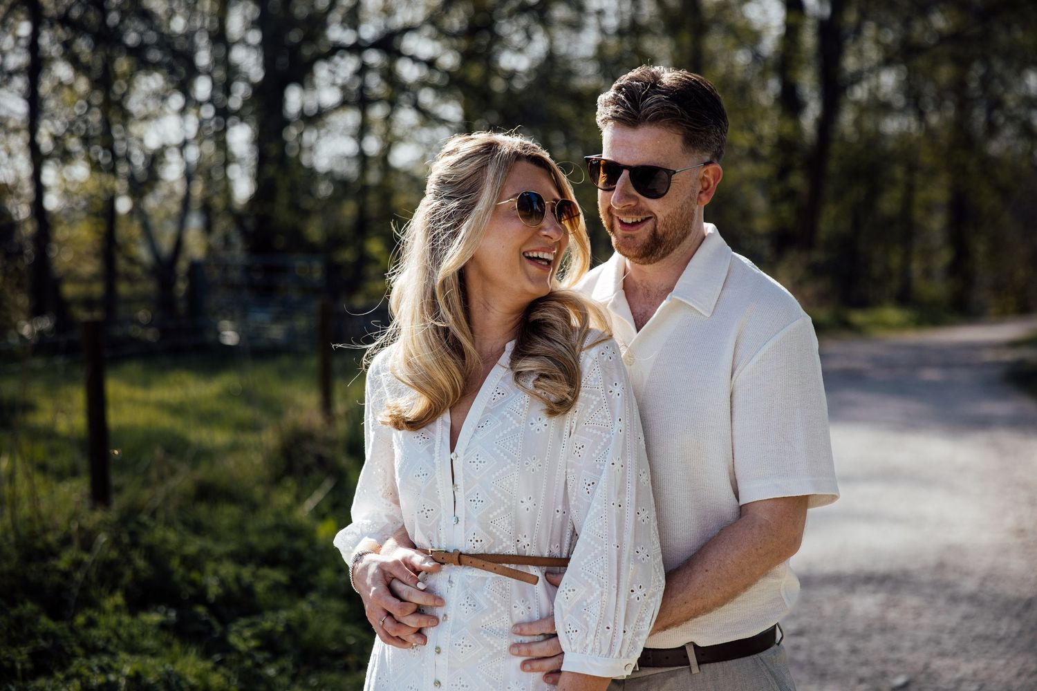 Joyful couple in white outfits share intimate moment during outdoor photoshoot.