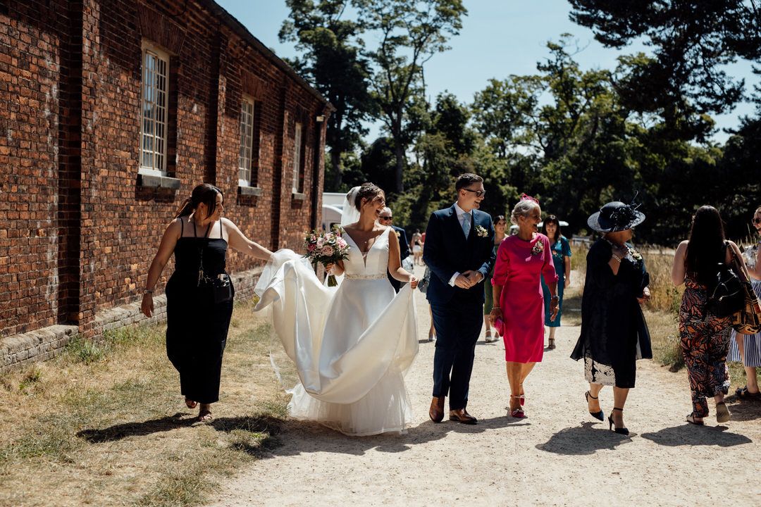 Wedding party walking along brick building exterior on sunny day.
