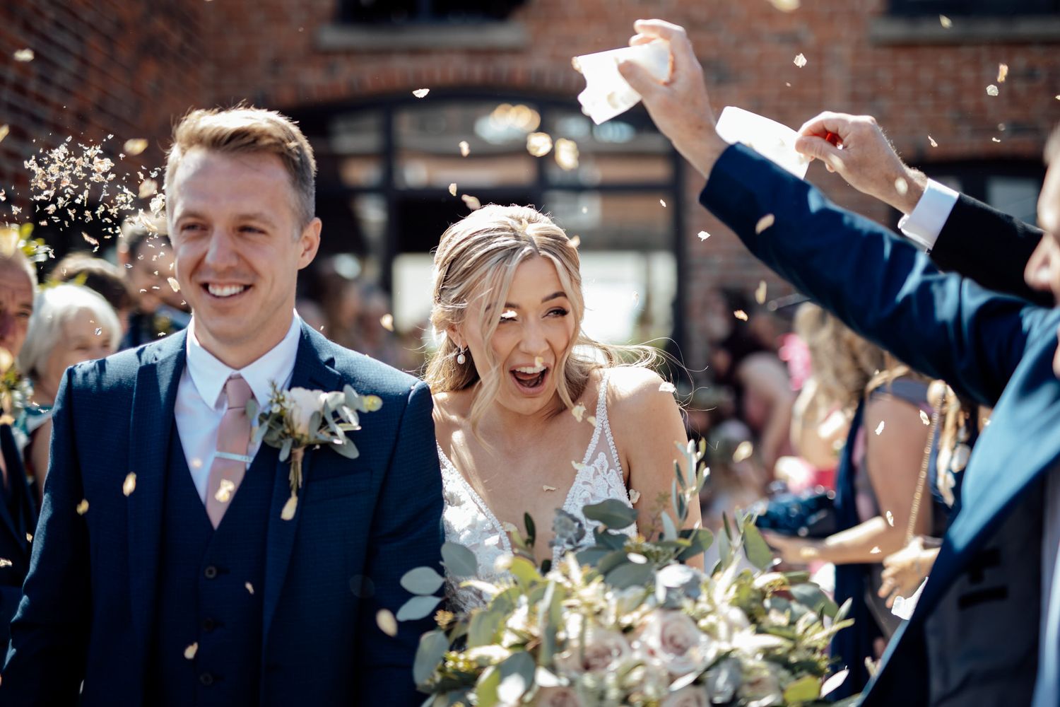 Joyful wedding celebration with confetti toss outside historic brick venue.
