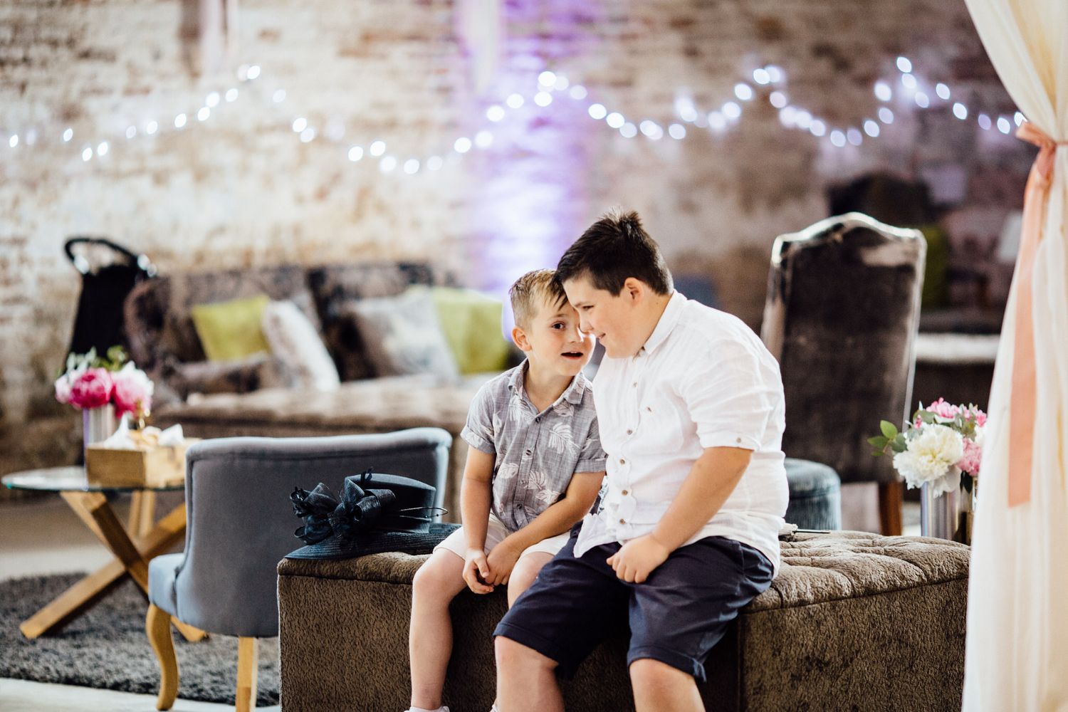 Two people share an intimate moment on a couch in a rustic brick venue with string lights.