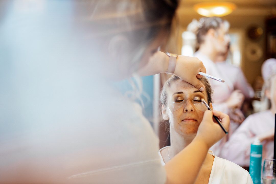 Professional makeup artist applies cosmetics during a bridal preparation session in warm lighting.