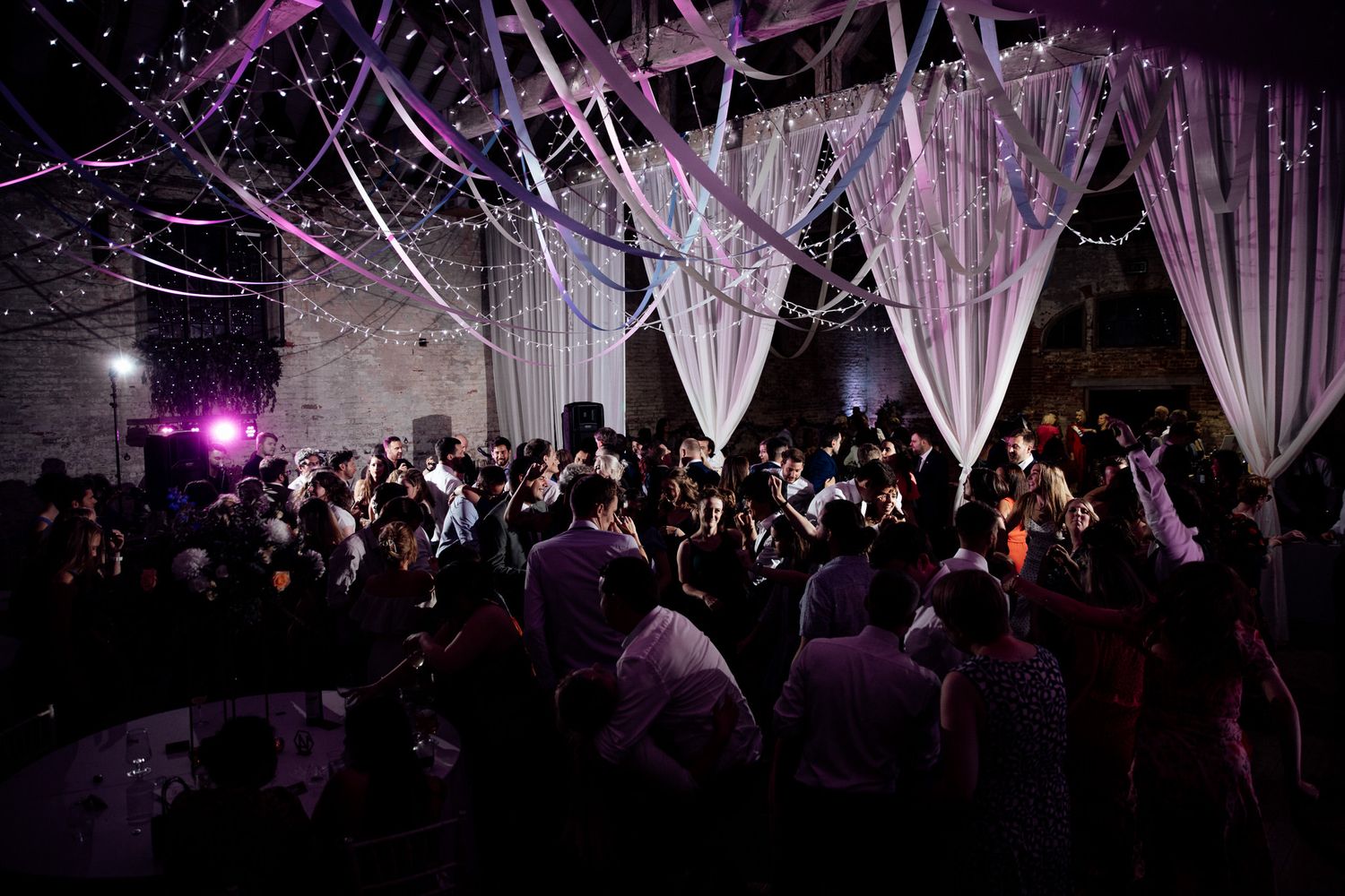 Dark reception venue illuminated by purple lights and hanging white fabric creating a dramatic atmosphere.