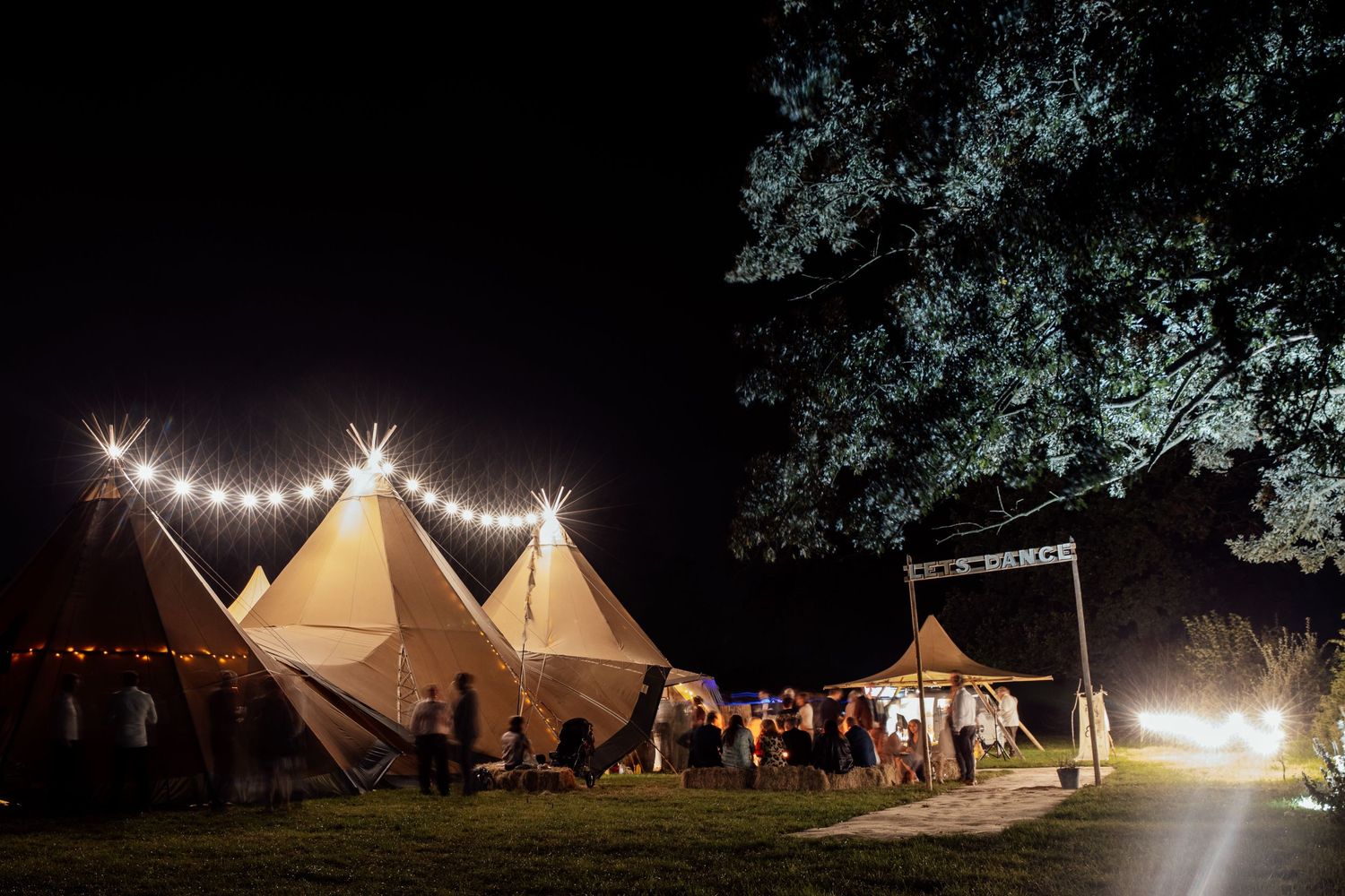 Illuminated white wedding tents glowing against the dark night sky at an outdoor reception venue.