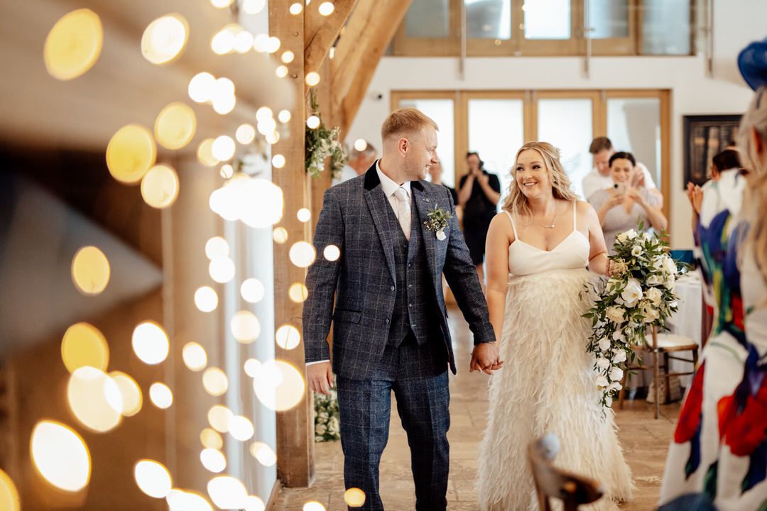 Newlyweds walking through venue decorated with string lights and wedding guests.
