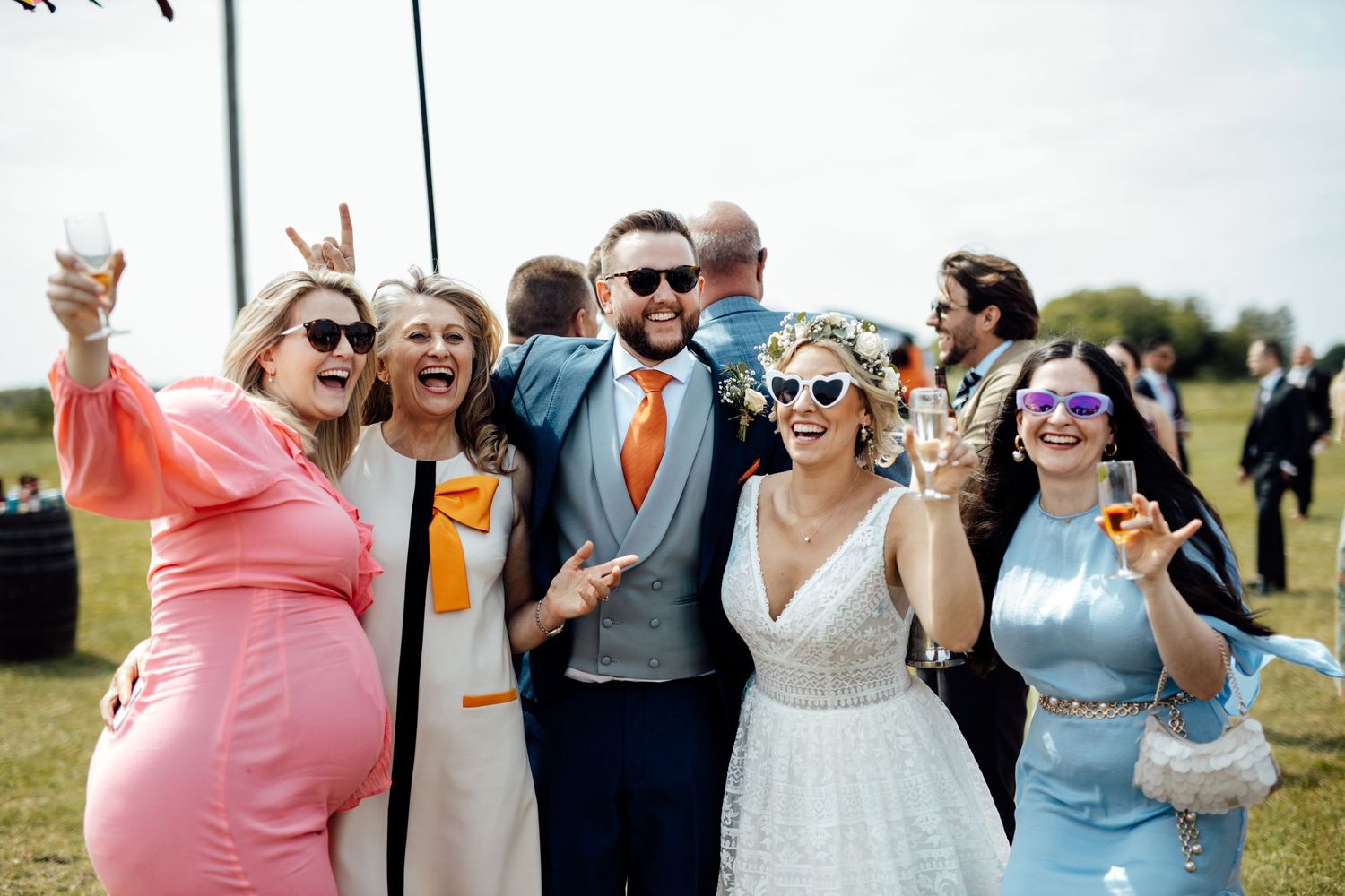 A celebratory group wearing colorful attire and sunglasses poses together outdoors.