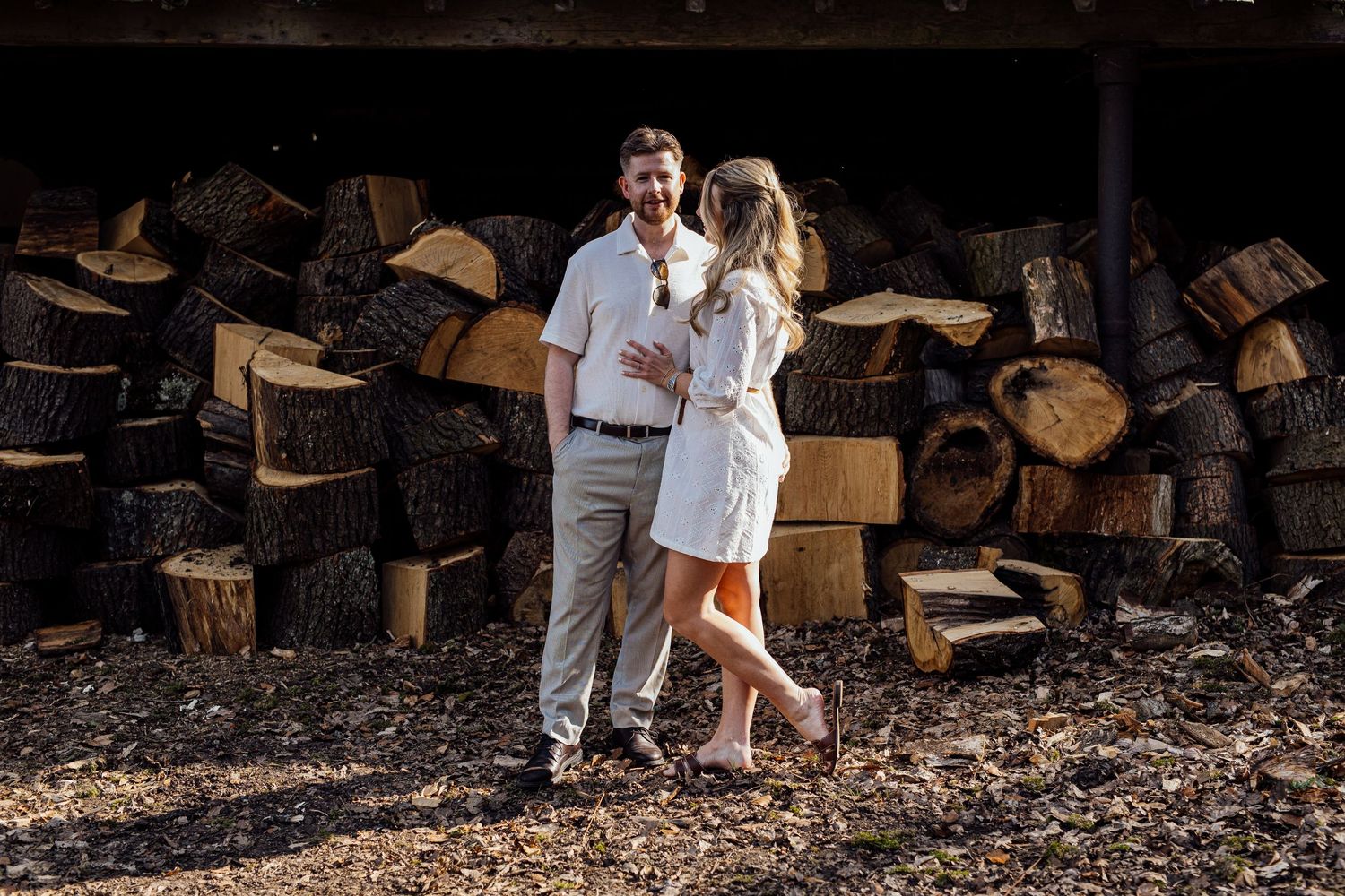 A romantic engagement photo session near stacked firewood at golden hour.