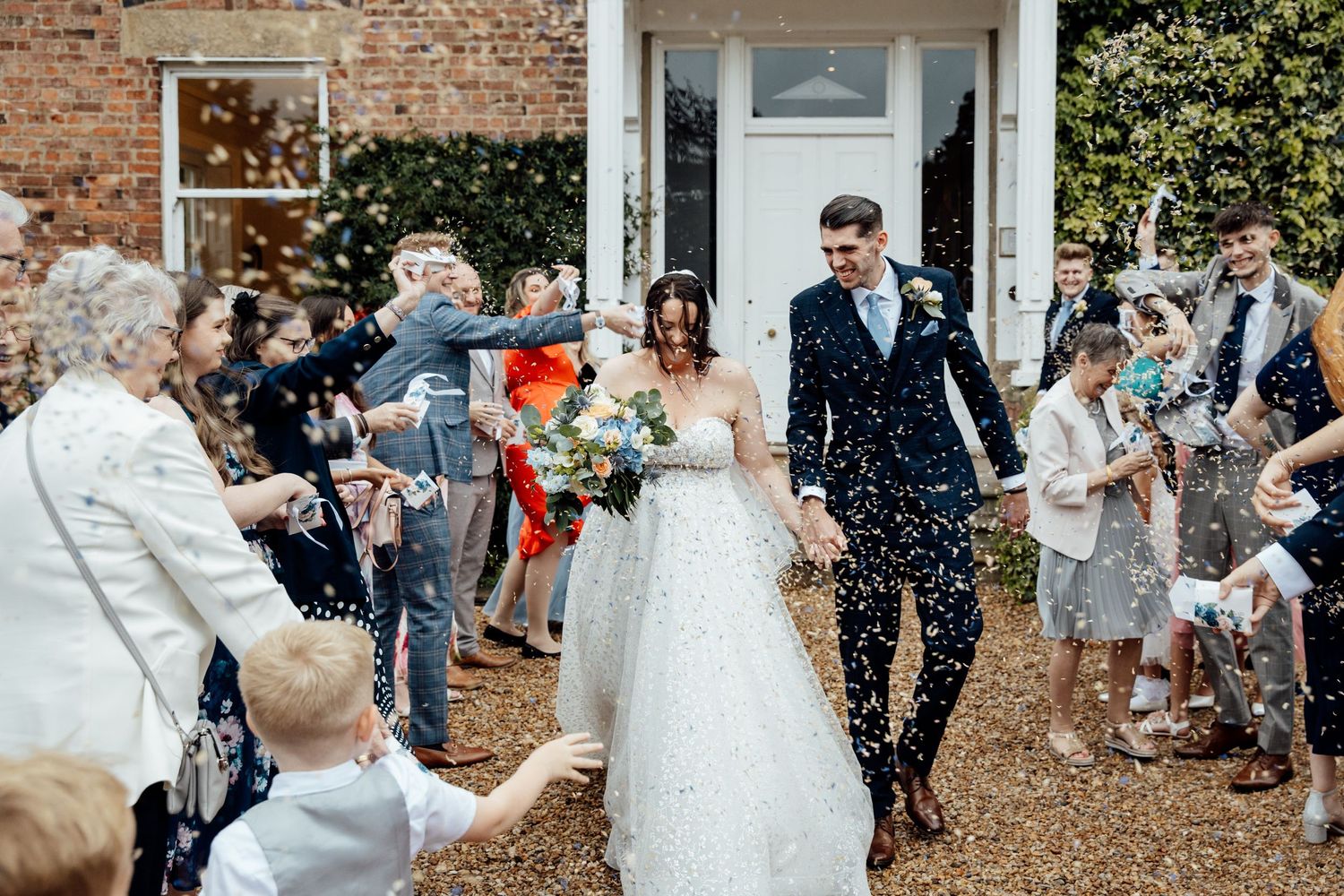 Wedding guests throwing confetti outside historic brick venue.