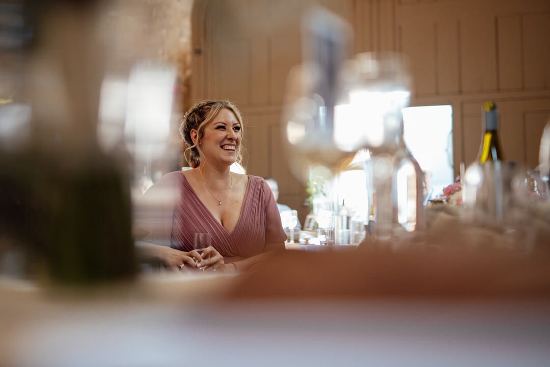 Candid moment captured at a wedding reception showing joyful laughter through wine glasses and table settings.