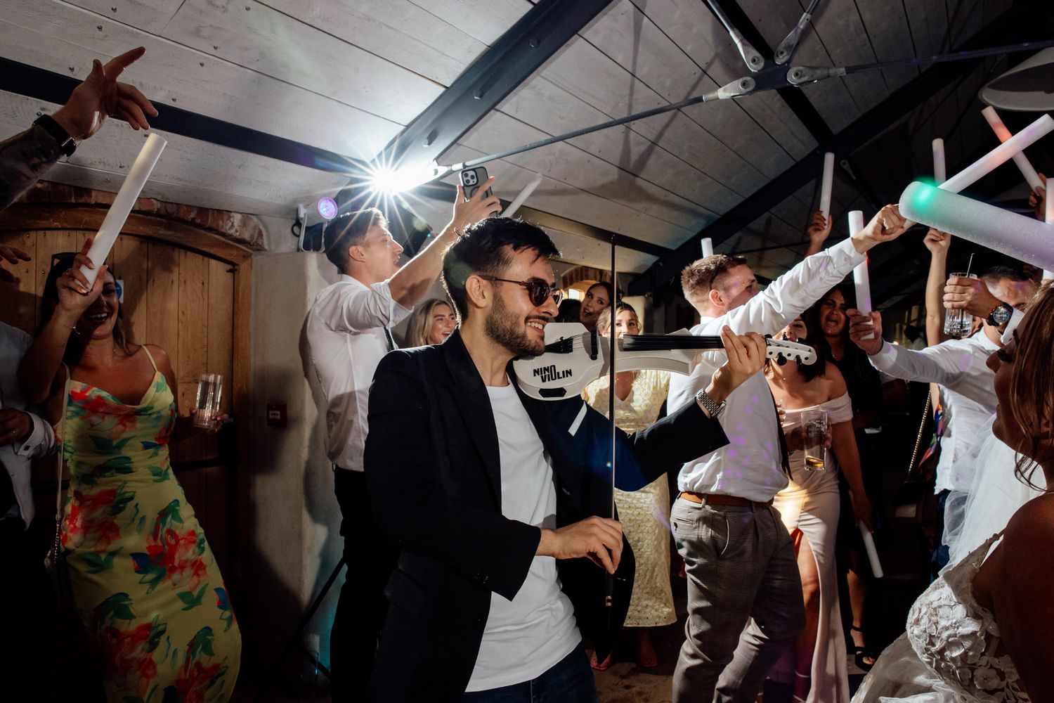 Wedding reception dance party with guests waving glow sticks on a dark dance floor.
