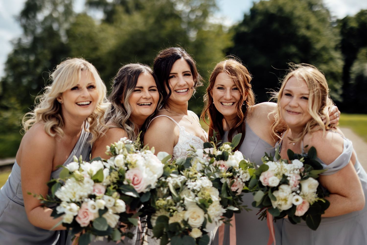 A bridal party holding beautiful bouquets of pink and white flowers outdoors.