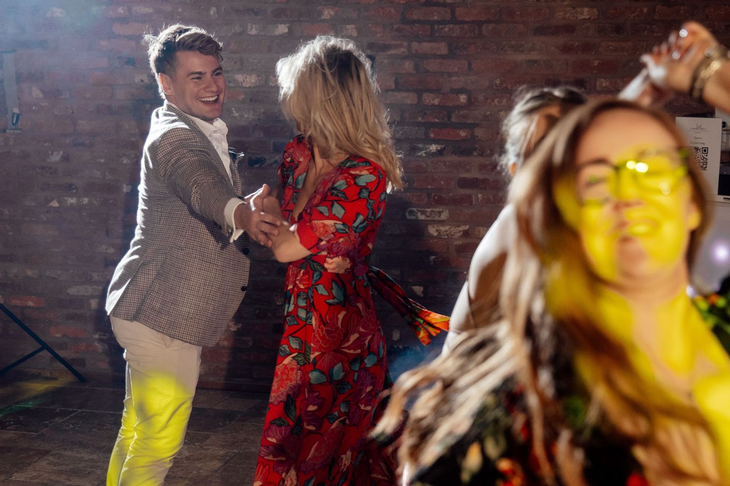 Wedding party dancing and celebrating on a rustic brick-walled dance floor.