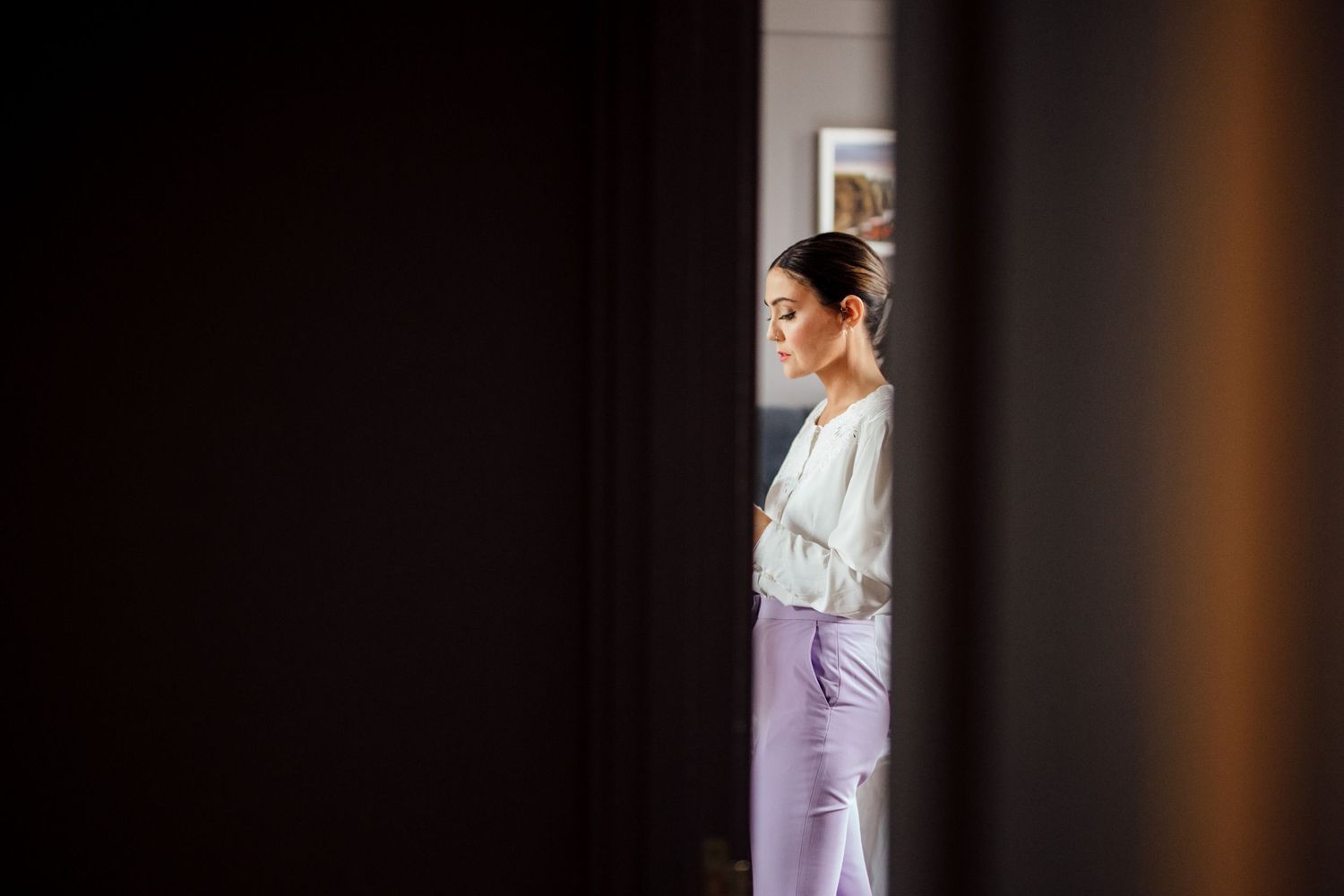 Side profile view through doorway of person wearing purple pants and white top.