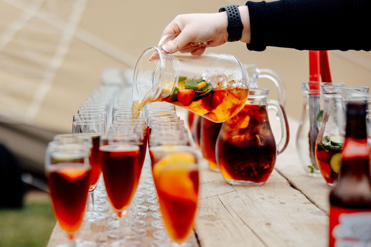 Hand pouring red sangria into glasses at an outdoor party.