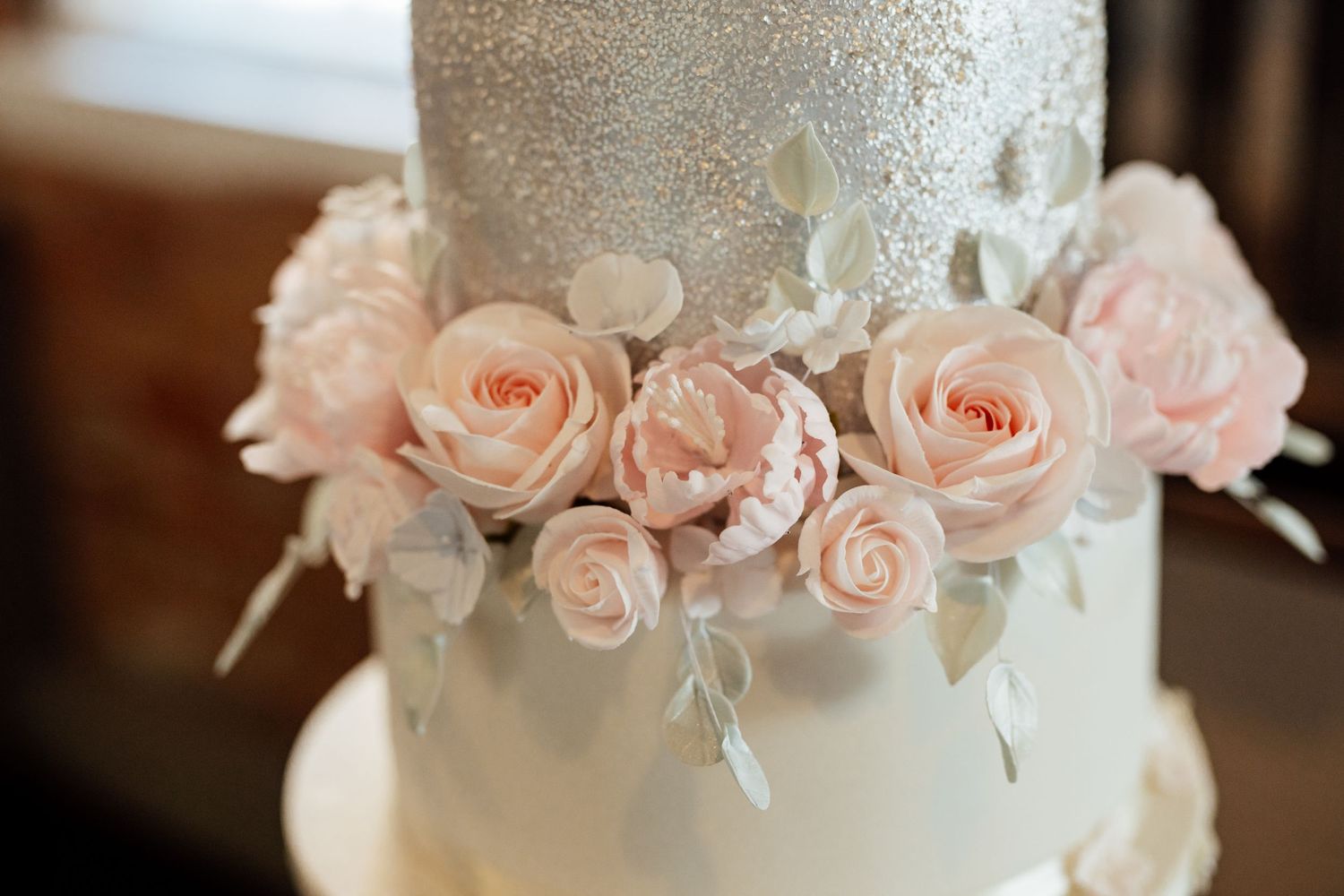 Wedding cake detail with delicate pink roses and silver accents on white fondant.