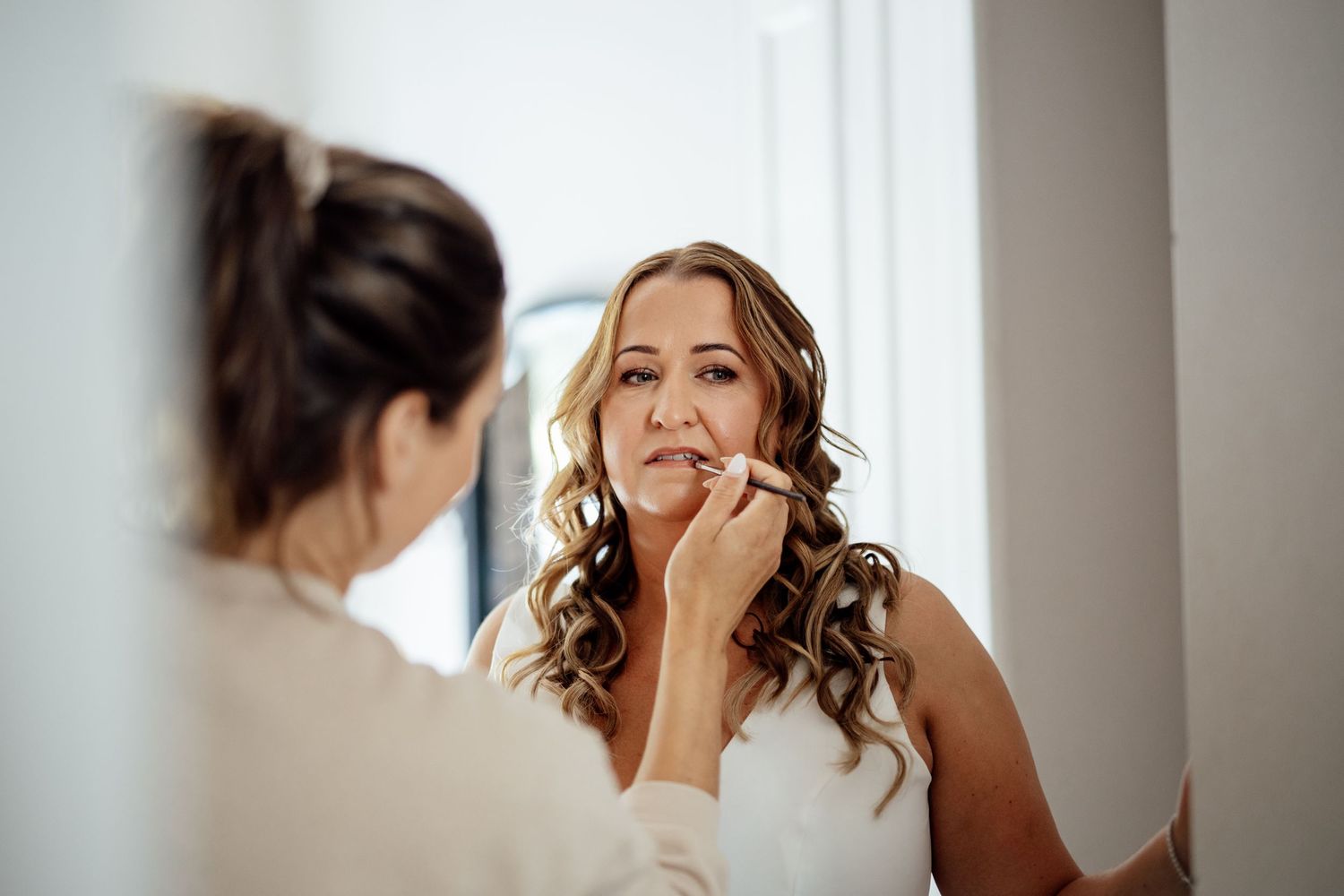 Bridal preparation moment captured in natural window light.
