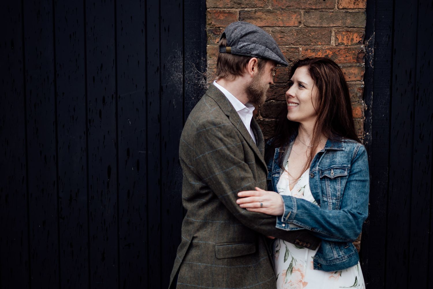A tender moment between a couple against a dark wooden wall and brick background.
