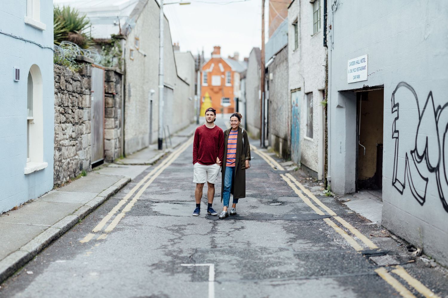Two figures walking down a narrow street between white buildings.