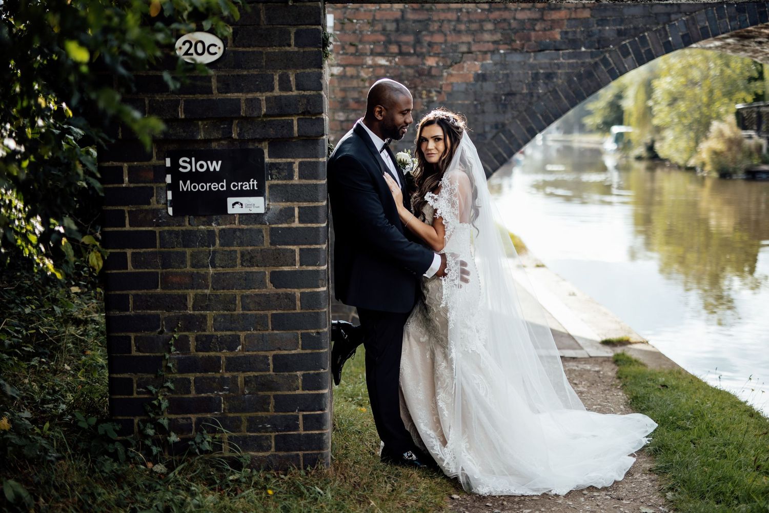 A romantic wedding portrait against a brick wall beside a serene waterway.