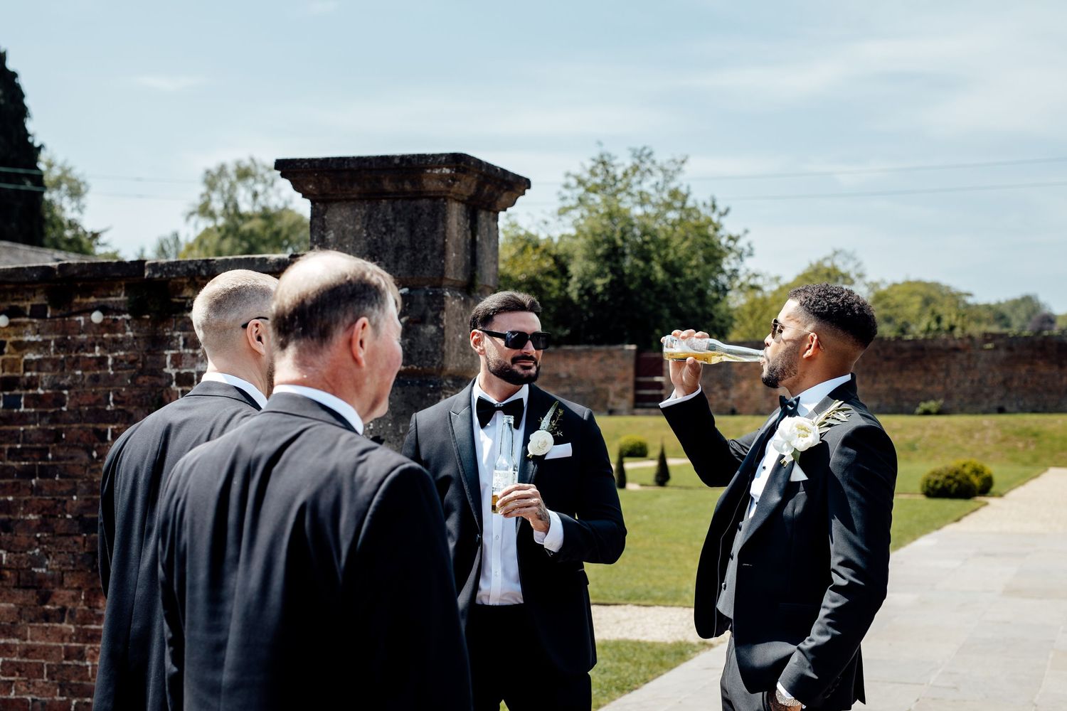 Wedding party members in formal attire gather outdoors on a sunny day.
