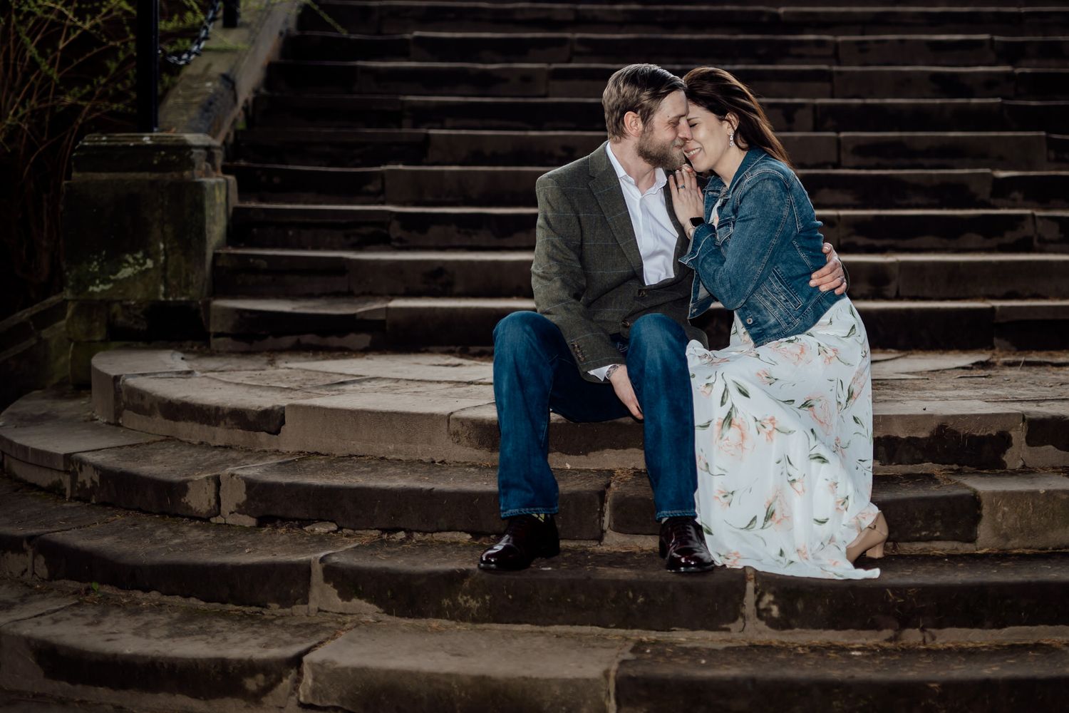 Couple sitting on stone steps in romantic engagement photoshoot at dusk.