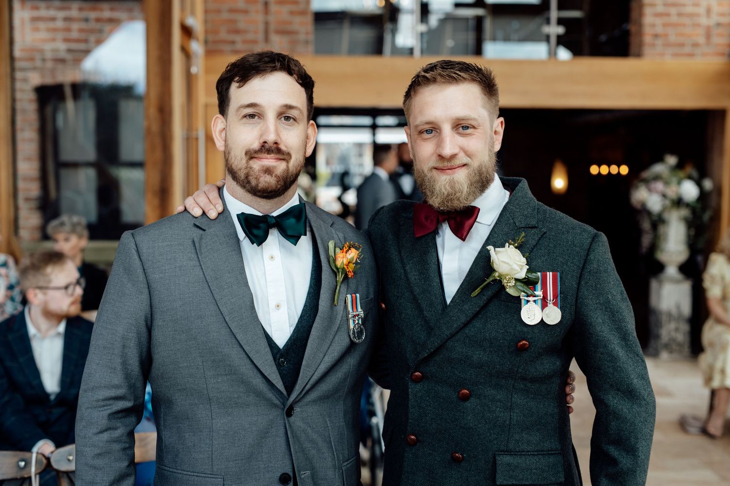 Groomsmen in formal black tuxedos pose together at a brick venue.