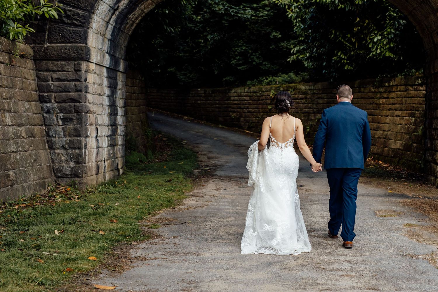 A couple walking down a stone-arched pathway surrounded by greenery.