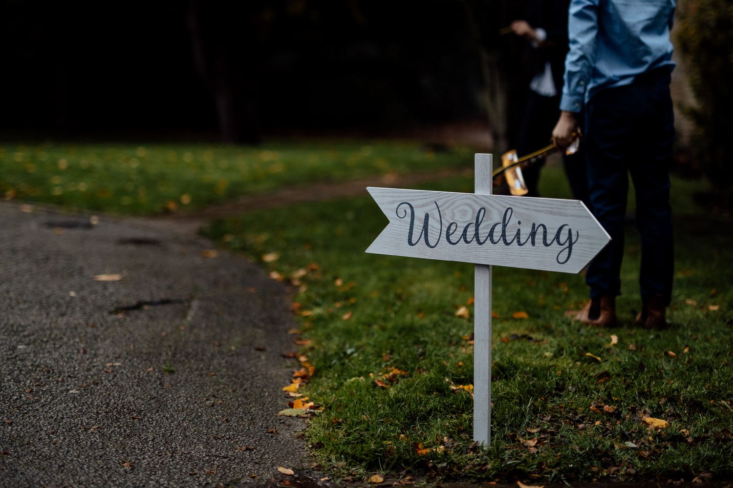 White wooden wedding directional sign stands among fallen autumn leaves.