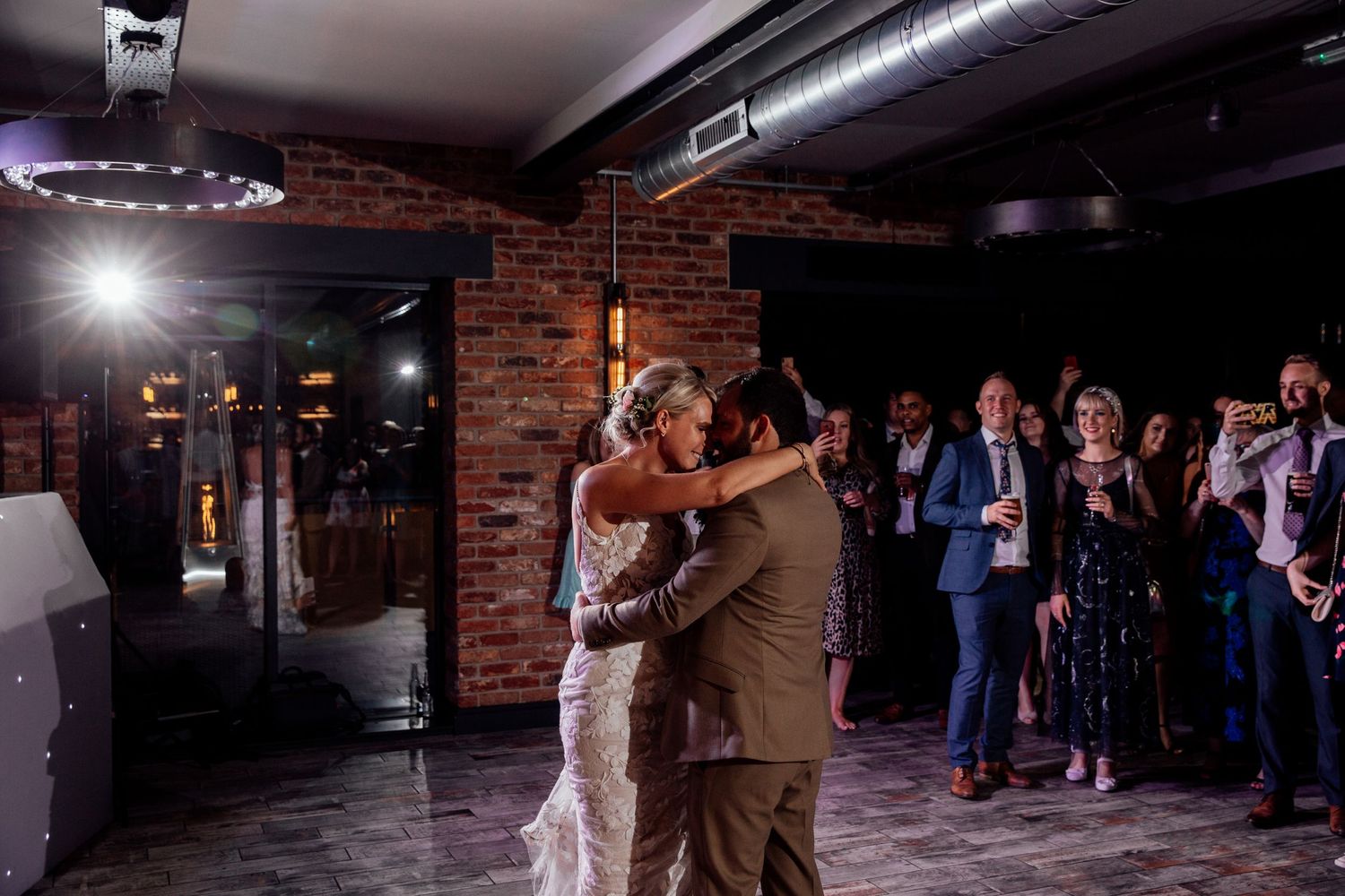 Wedding dance floor moment captured in a dimly lit industrial venue with brick walls.