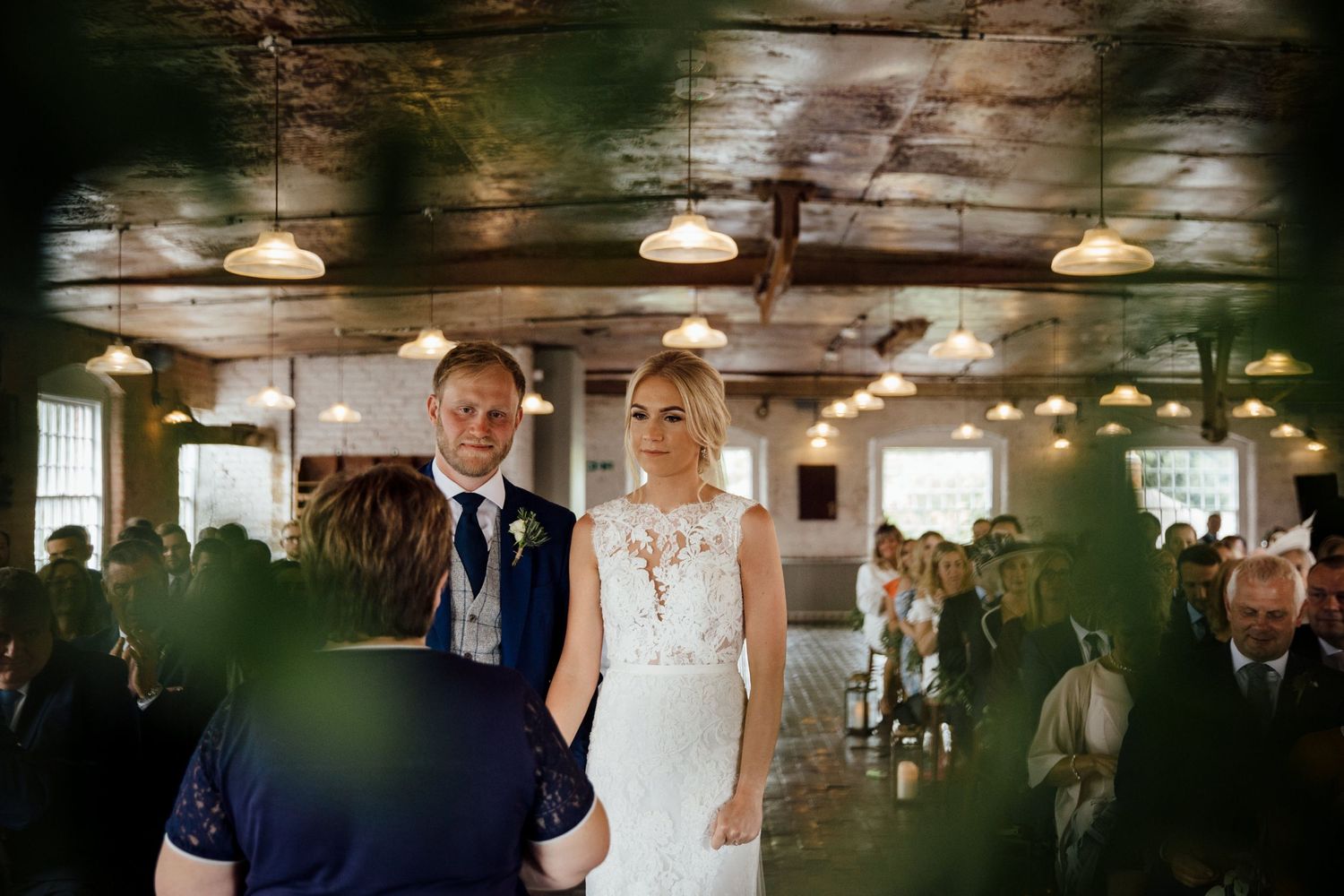 Wedding ceremony in a rustic industrial space with exposed brick walls and overhead lighting.