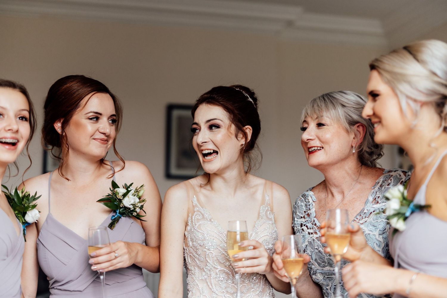 Bridesmaids in lavender dresses sharing champagne and laughter with the bride.