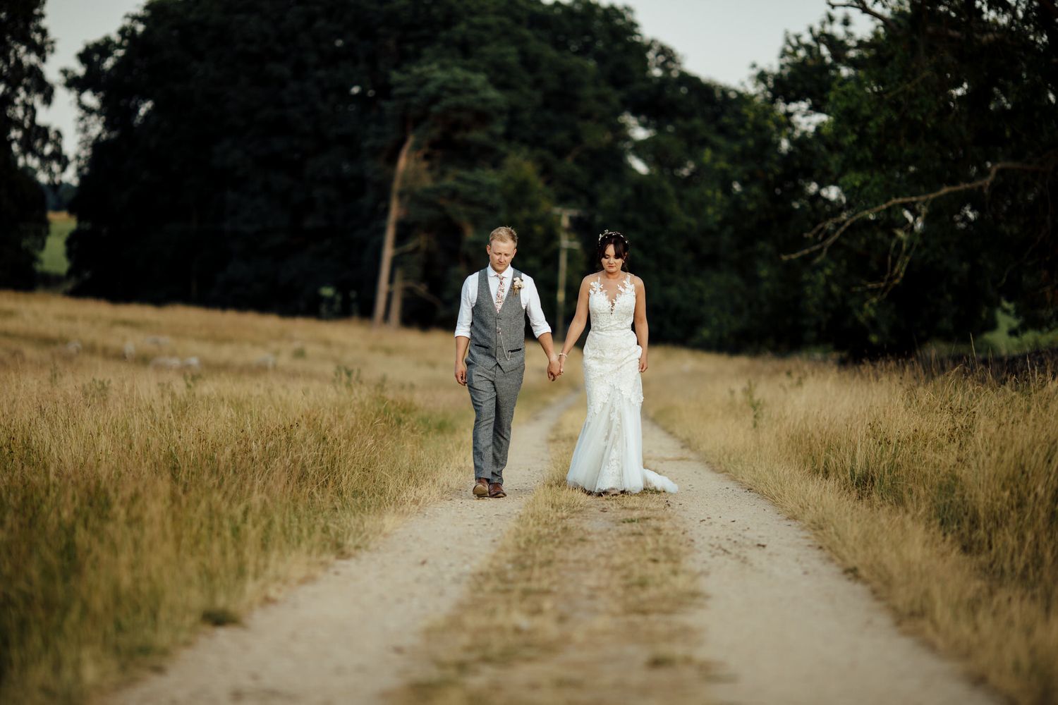 Couple walking together on a dirt path through a golden meadow.