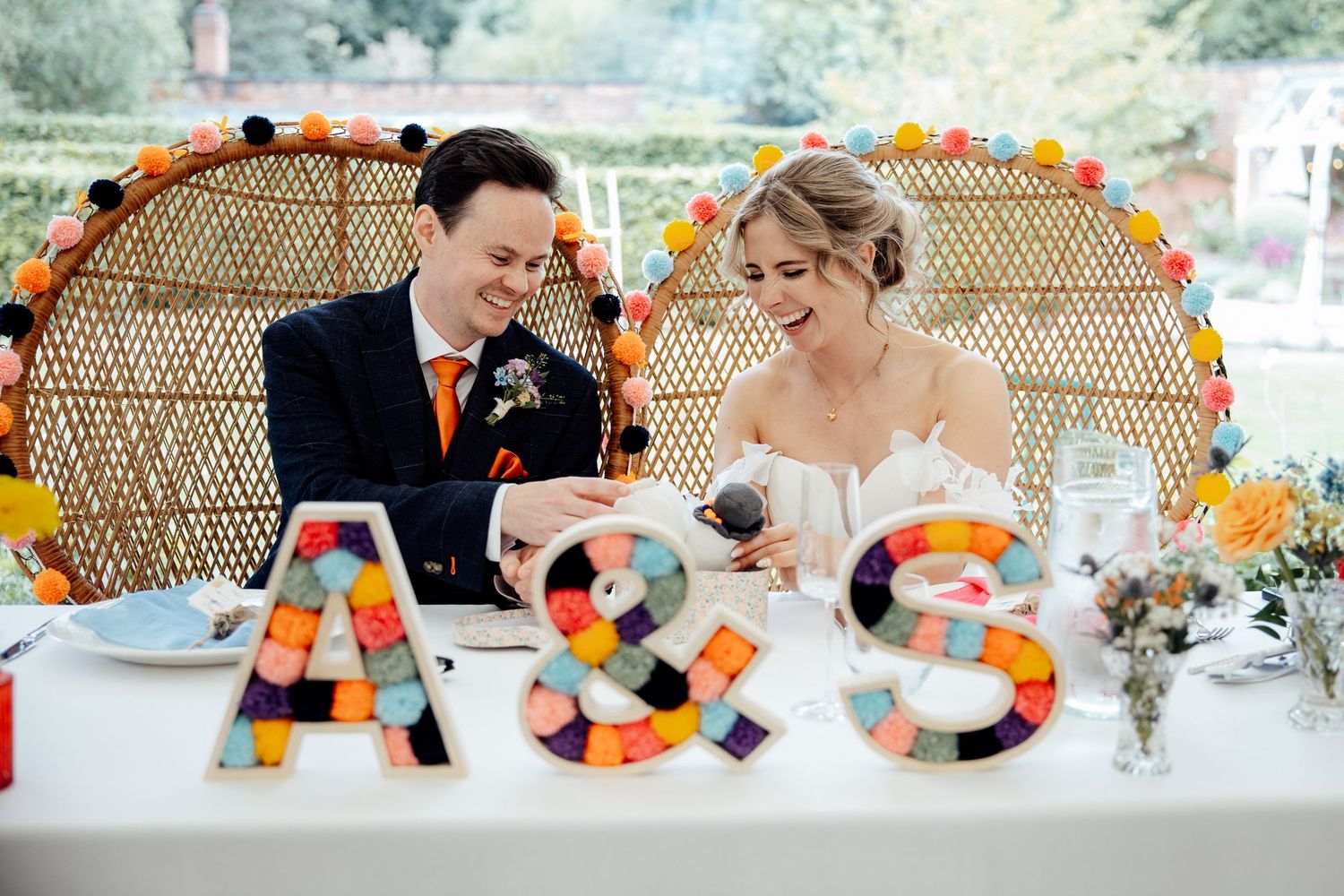 Wedding reception table decorated with colorful rainbow decor and peacock chair at an outdoor celebration.